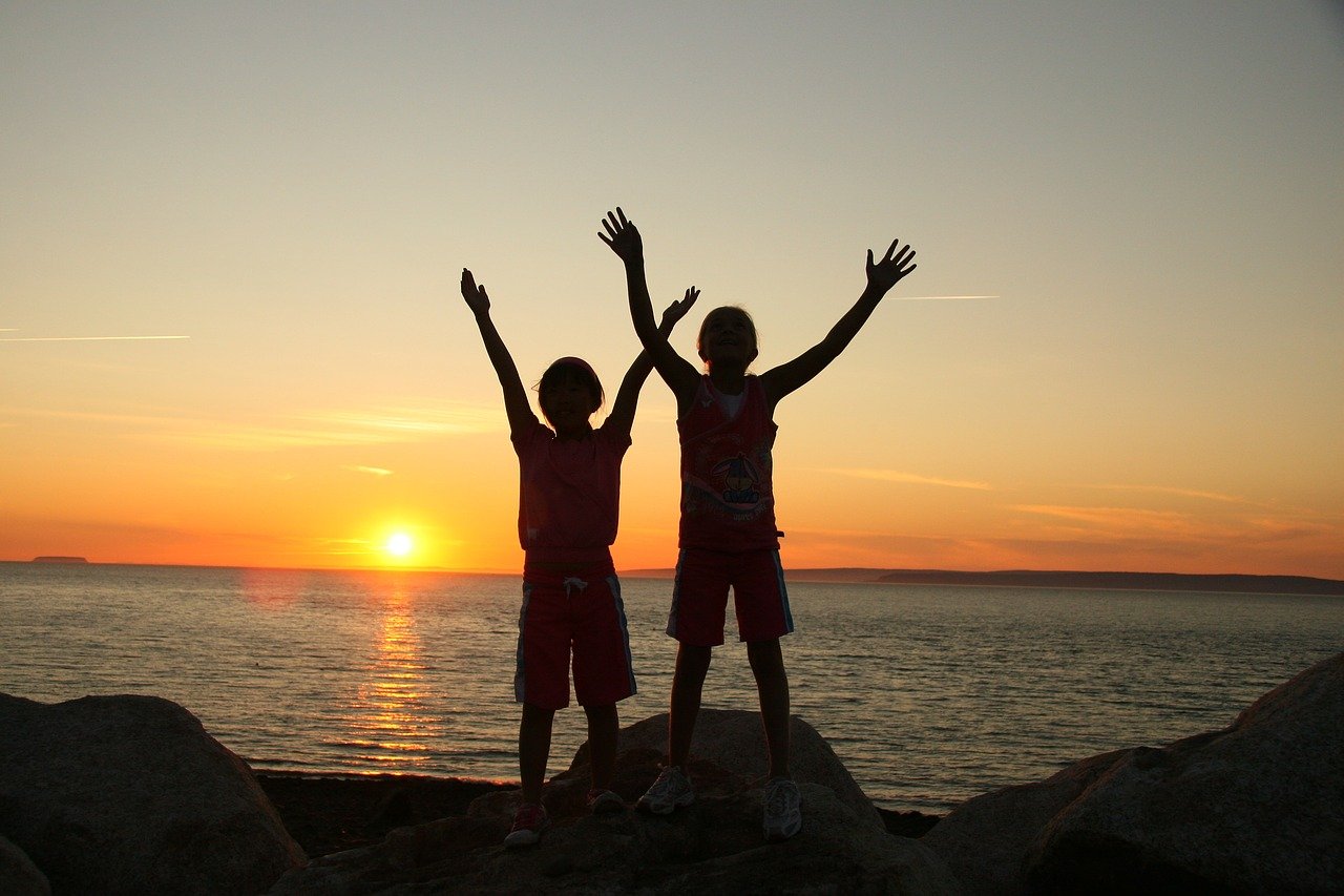 two children raising hands with the sunset behind them